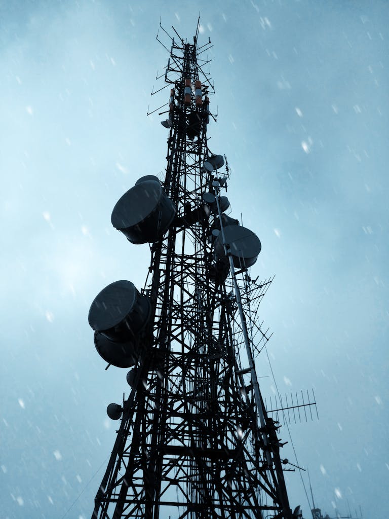 Low angle view of a telecommunication tower silhouetted against a dramatic, cloudy sky.